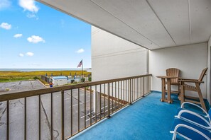 A balcony with a view of the beach, a flag, and a table with chairs.