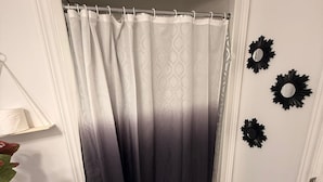 A bathroom with a white toilet, a black and white patterned rug, a grey gradient shower curtain, and three black wall decorations. - Serenity Space (Niagara Falls)