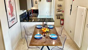 Une cuisine moderne avec une table à manger pour quatre personnes, des chaises transparentes, un réfrigérateur, une cuisinière à gaz et un luminaire suspendu.