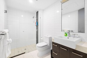 A modern bathroom with a white toilet, a glass shower enclosure, and a vanity with a mirror. - Beaufort Street 1bdr Parking (Perth)