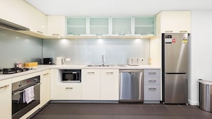 A modern kitchen with white cabinets, a stainless steel refrigerator, a dishwasher, an oven, and a microwave. - Beaufort Street 1bdr Parking (Perth)