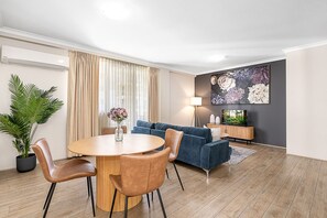 A modern living room with a round dining table, blue sofa, and a flat-screen TV. - 2bdr East Perth Getaway (Perth)