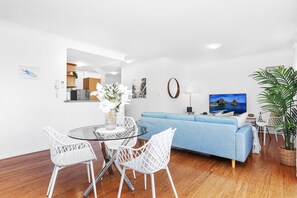 Ein modernes Wohnzimmer mit einem Glastisch, weißen Stühlen, einem blauen Sofa und einer großen Topfpflanze.
