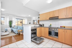 A modern kitchen with wooden cabinets, stainless steel appliances, and a dishwasher. - Modern 2BR Pool Gym Parking (Perth)