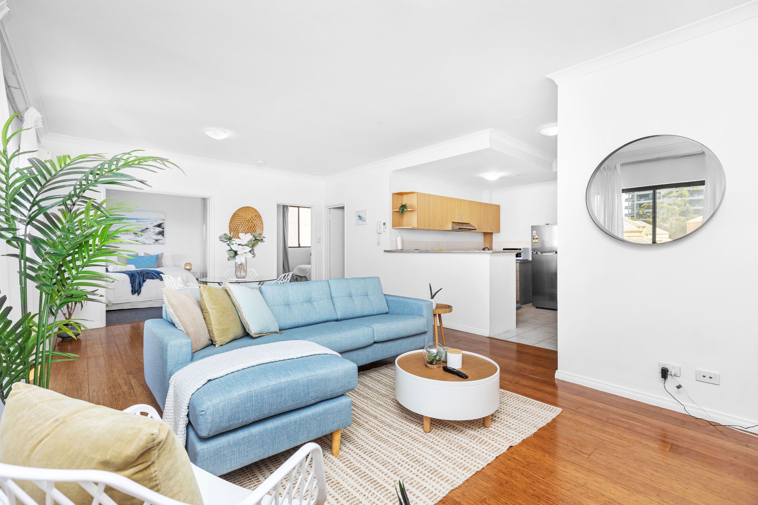 A modern living room with a blue sofa, a round coffee table, and a large mirror on the wall.