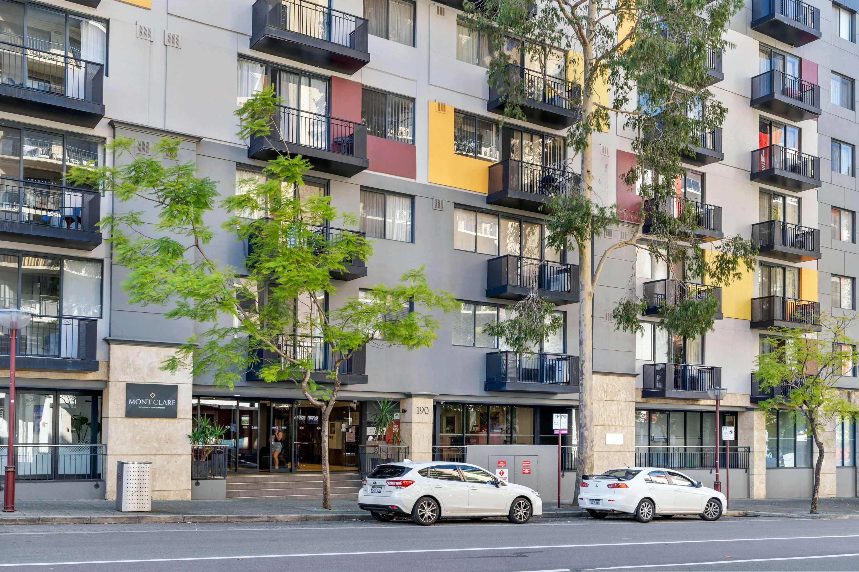 Um edifício com várias andares, varandas, uma fachada comercial e carros estacionados.