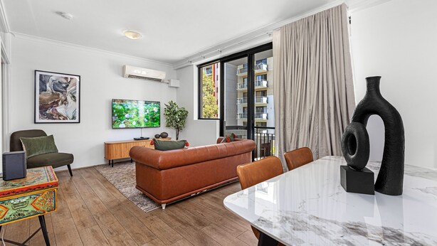 A modern living room with a sofa, a dining table, and a TV. - Stunning 1bdr Paradise - Gym Pool (Perth)