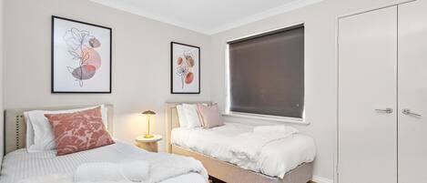 A bedroom with two beds, a wardrobe, and artwork on the walls.