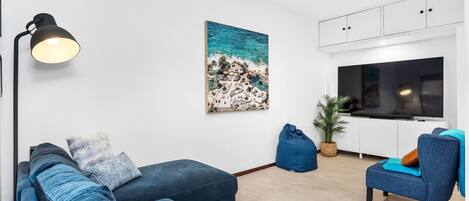 A modern living room with a sofa, a bean bag, a TV, and a painting of a beach scene.