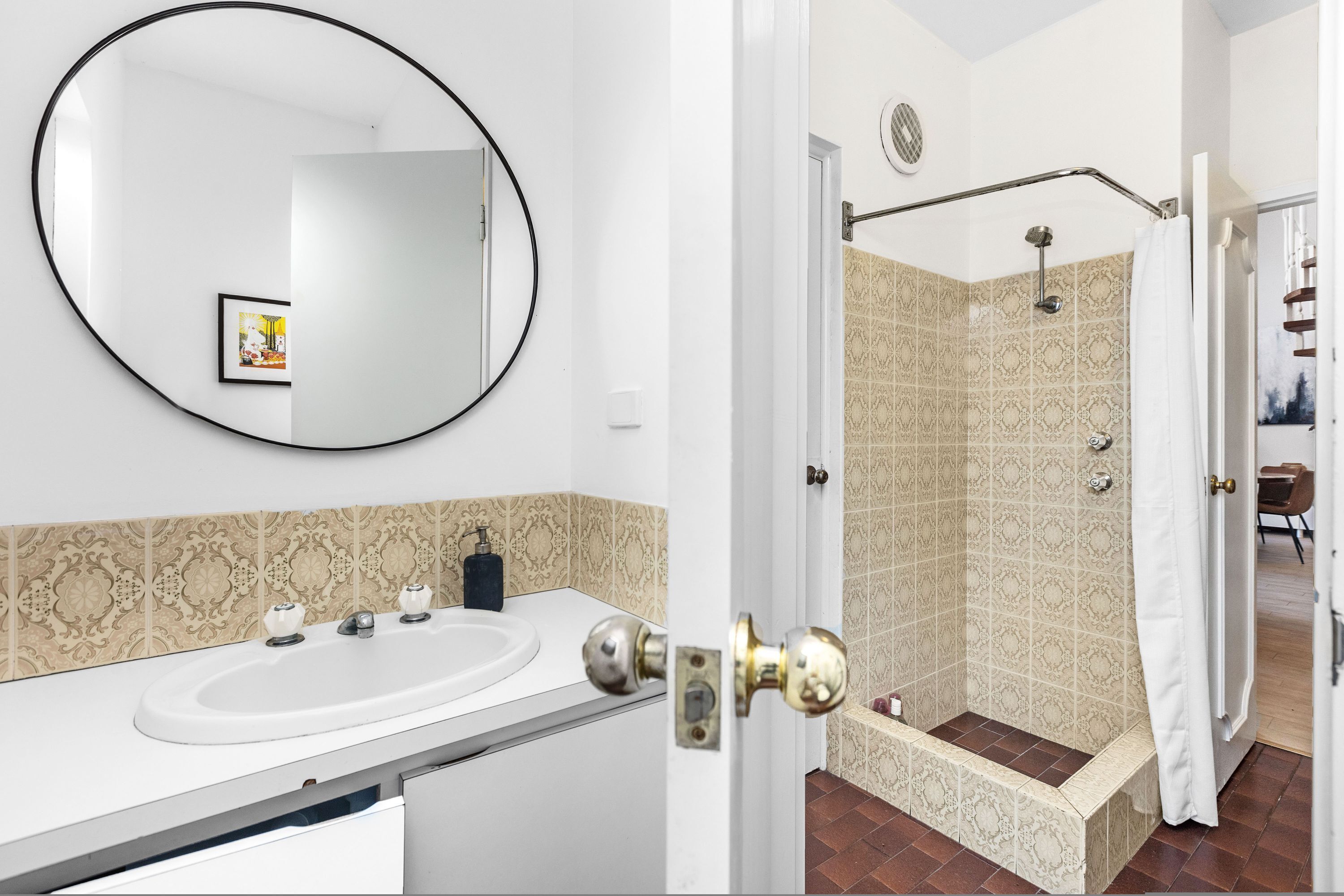 A bathroom with a white sink, a round mirror, and patterned tiles.