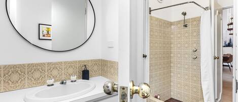 A bathroom with a white sink, a round mirror, and patterned tiles.
