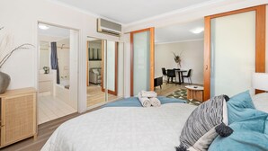 A hotel room with a bed, a small table, and a chair. There is a bathroom visible through an open door. - Spacious 1bdr Fast Wi-fi Near RAC Arena (Perth)