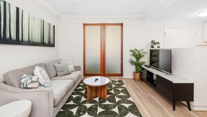 A modern living room with a sofa, coffee table, TV, and a large painting on the wall. - Spacious 1bdr Fast Wi-fi Near RAC Arena (Perth)