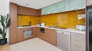 A modern kitchen with wooden cabinets, a stainless steel dishwasher, and a yellow backsplash. - 1bdr Parking on Beaufort Street (Perth)