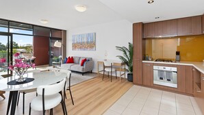 A modern kitchen with wooden cabinets, a built-in oven, and a dining area with a white table and chairs. - 1bdr Parking on Beaufort Street (Perth)
