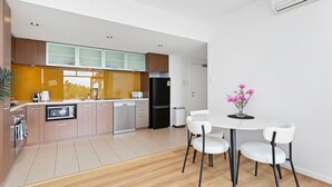 A modern kitchen with wooden cabinets, a black refrigerator, and a white dining table with four chairs. - 1bdr Parking on Beaufort Street (Perth)