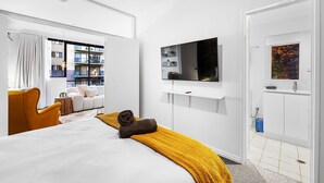 A modern hotel room with a bed, a TV mounted on the wall, a balcony with a sofa, and a view of the cityscape. - Bespoke East Perth - Sleeps 2 - Superior Wifi (Perth)