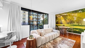 A modern living room with a large window, a sofa, a dining table, and a mural of a park. - Bespoke East Perth - Sleeps 2 - Superior Wifi (Perth)