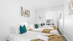 A hotel room with two beds, white bedding, teal pillows, and a large mirror. - Modern 2BR Pool Gym Parking (Perth)