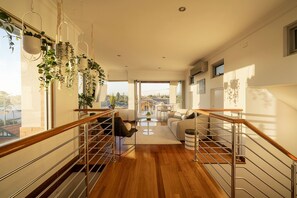 A spacious living area with a wooden staircase, a sofa, a coffee table, and hanging plants. - Designer Luxury 3brd - Epic Views - South Perth (Perth)