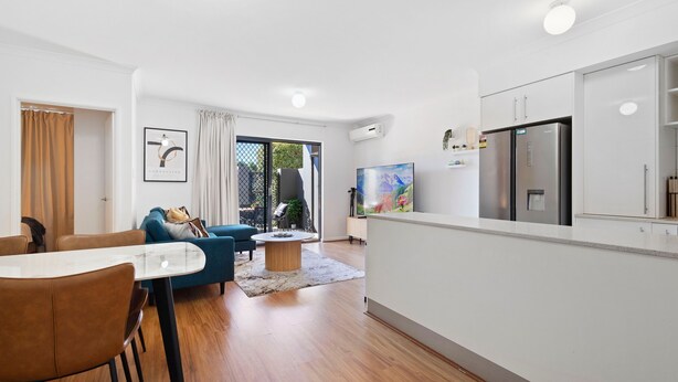 A modern living room with a dining area, a kitchen with white cabinets, and a large window with curtains. - Perfect Location 2BR 1bth - Beckenham (Perth)