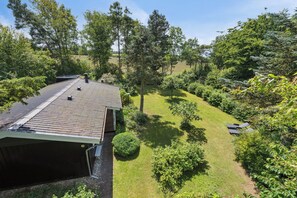 Une maison avec un toit en pente, entourée d’une pelouse bien entretenue et d’arbres touffus.