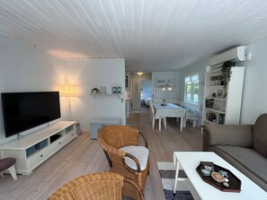 A living room with a TV, wicker chairs, a white sofa, and a dining area with a table and chairs.