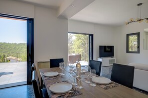 A dining area with a table set for four, a television on a stand, and a view of a balcony with outdoor furniture. - Stylish air-conditioned villa in a privileged area of Biot just minutes from sea (Biot)