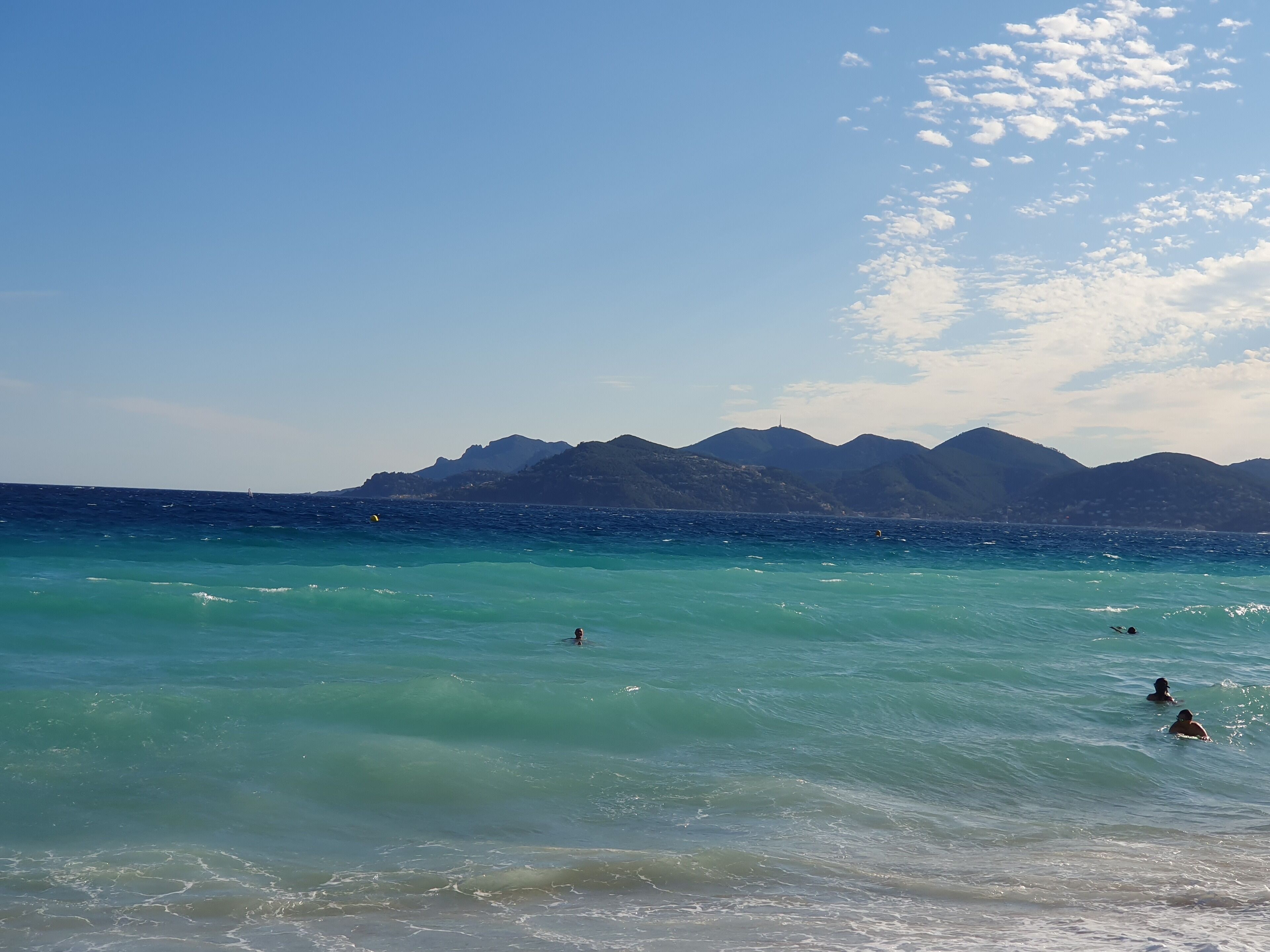 A beach with clear turquoise water and distant mountains.