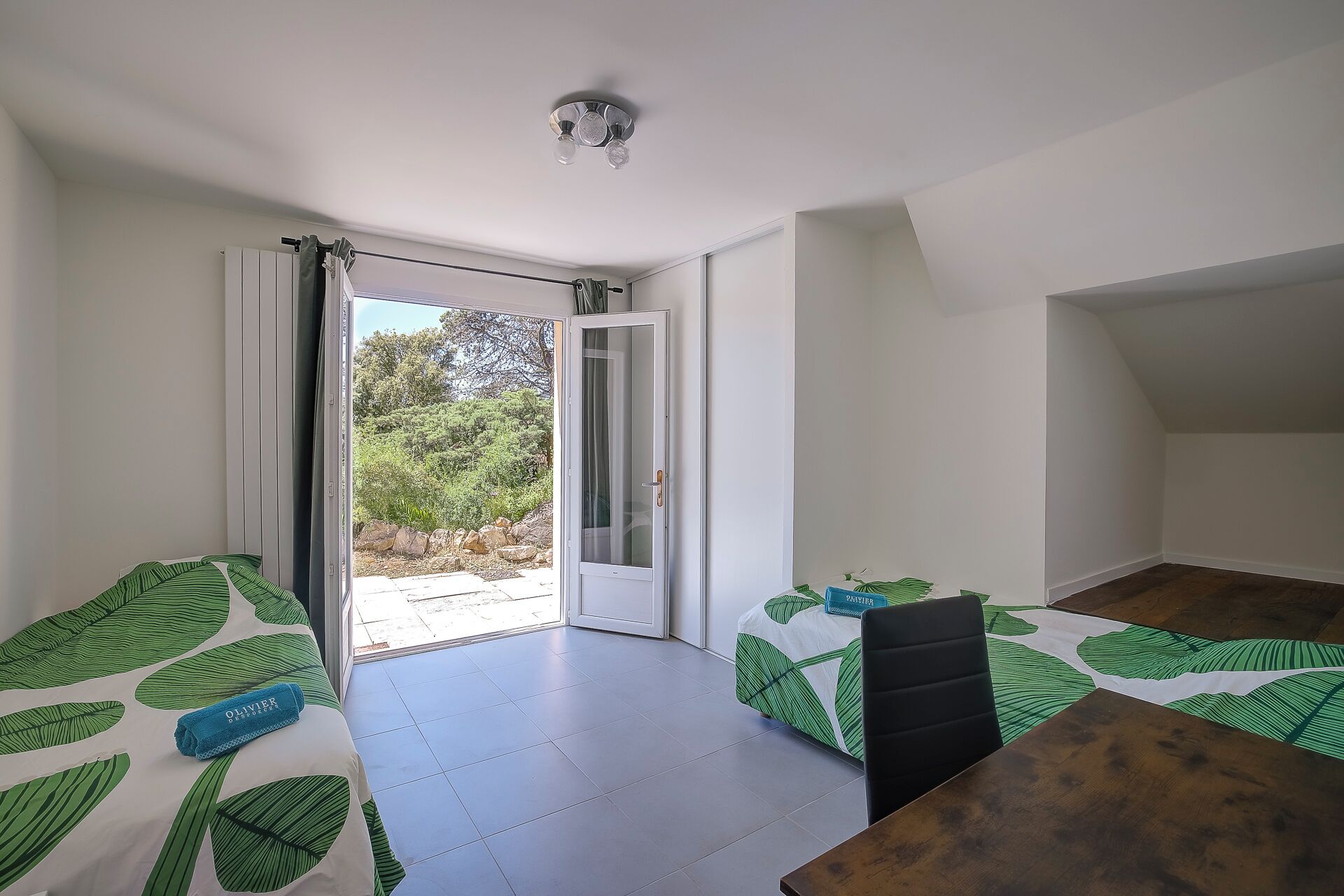 A room with a bed, a table, and a view of a garden through a sliding door.