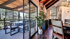 A modern kitchen with a clock, wooden ceiling, and a dining area with a glass door overlooking a deck.