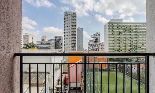 A high-rise building with multiple balconies, a fenced sports field, and a clear sky. - Modern Studios 500m From the Metro in Pinheiros - CPM (São Paulo)