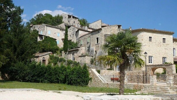 A stone building with multiple levels, a palm tree in the foreground, and a clear blue sky. - ZEcamping 4* familial piscine chauffée dog friendly locatif TV LV clim (Rochegude)
