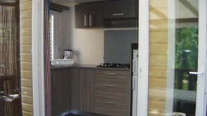 A compact kitchen with wooden cabinets, a gas stove, and a refrigerator. - ZEcamping 4* familial piscine chauffée dog friendly locatif TV LV clim (Rochegude)
