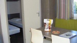 A room with a bunk bed, a table with a bag and a book, and a window with curtains. - ZEcamping 4* familial piscine chauffée dog friendly locatif TV LV clim (Rochegude)