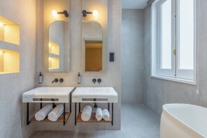 A modern bathroom with two sinks, a mirror, and a bathtub. There are towels on the sinks and a window with a view. - FORTINN Puerta del Sol (Madrid)