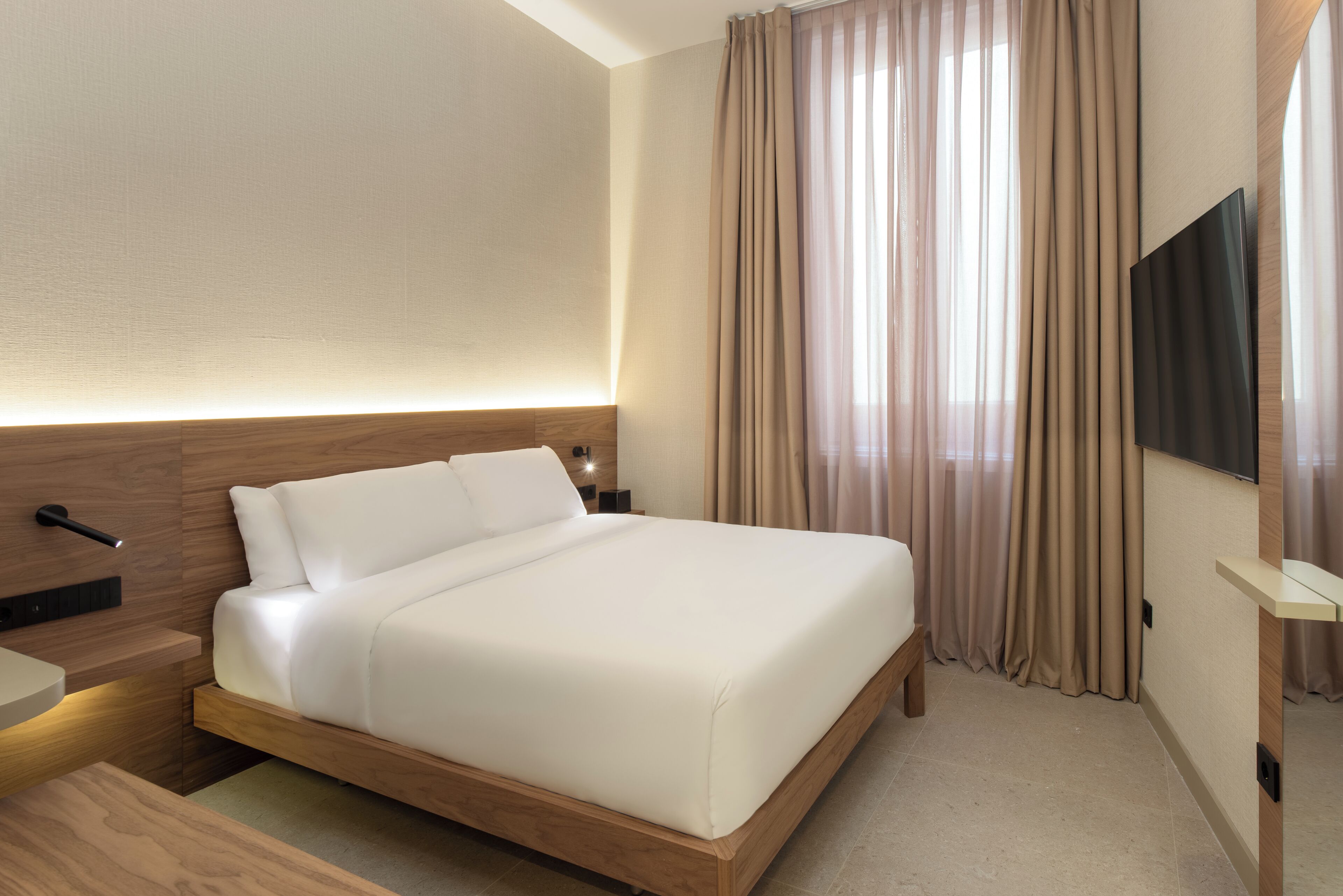 A hotel room with a large bed, wooden headboard, a flat-screen TV, and a bedside table.