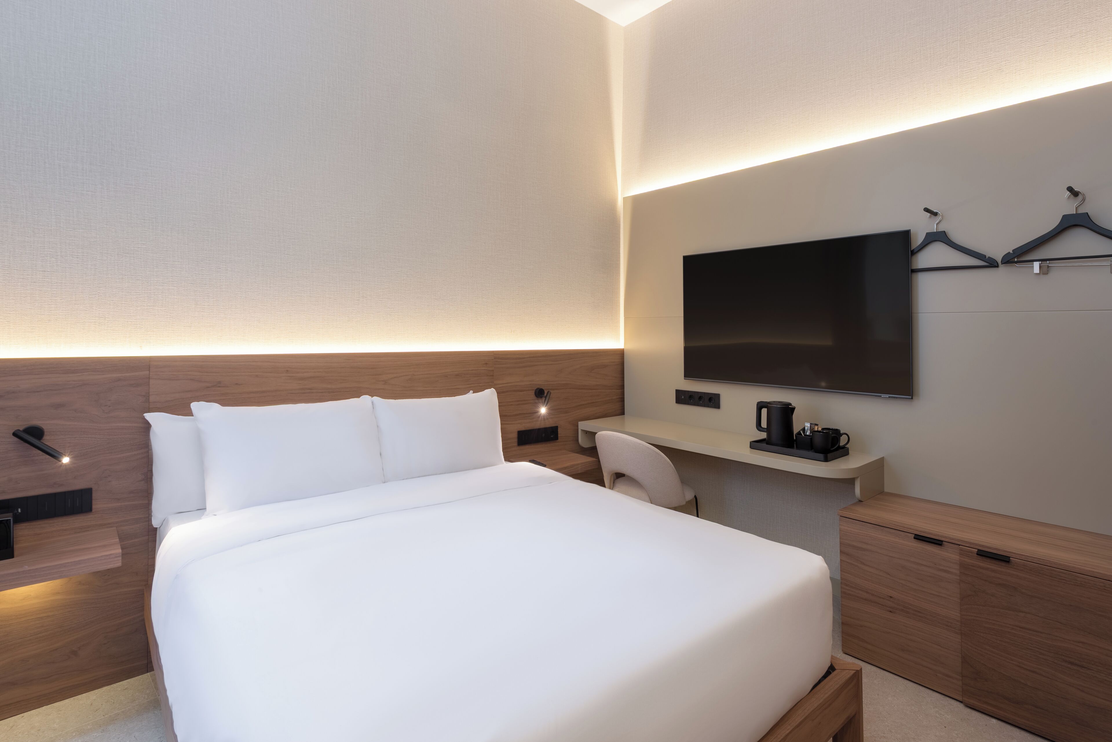 A modern hotel room with a large bed, a desk, a flat-screen TV, and a coffee maker.
