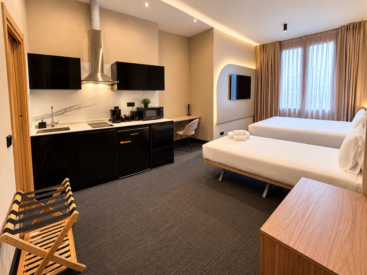 A hotel room with a kitchenette, a bed, a desk, and a chair.