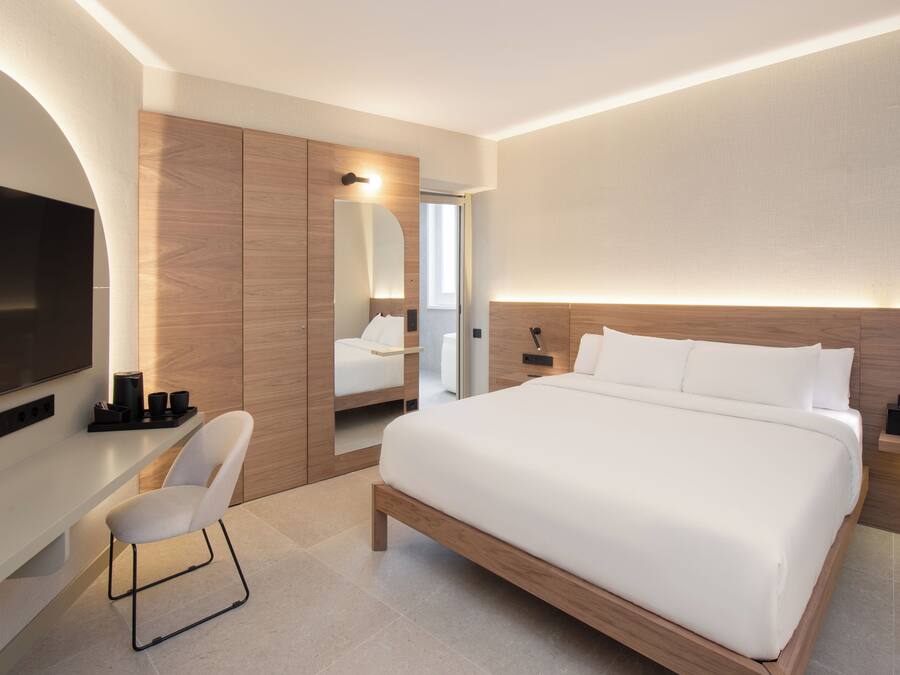 Una habitación de hotel moderna con una cama grande, un televisor de pantalla plana, una zona de estar y un vestidor.