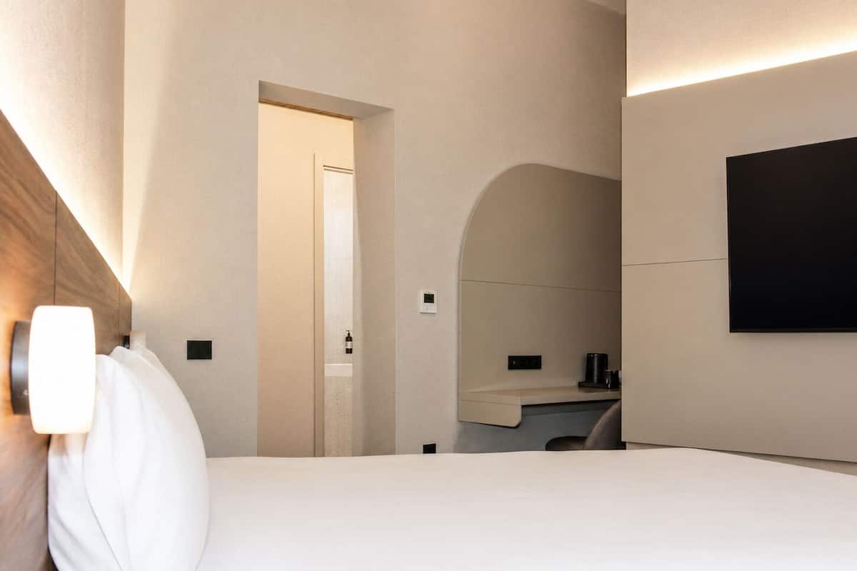A hotel room with a bed, a nightstand, a mirror, and a wall-mounted TV.