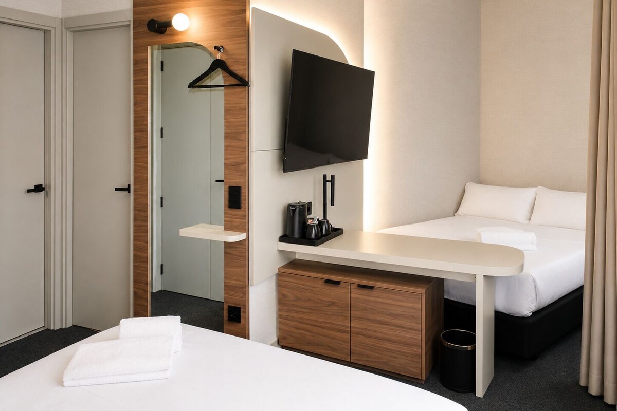Een hotelkamer met een bed, nachtkastje, televisie, houten kast en een spiegel.