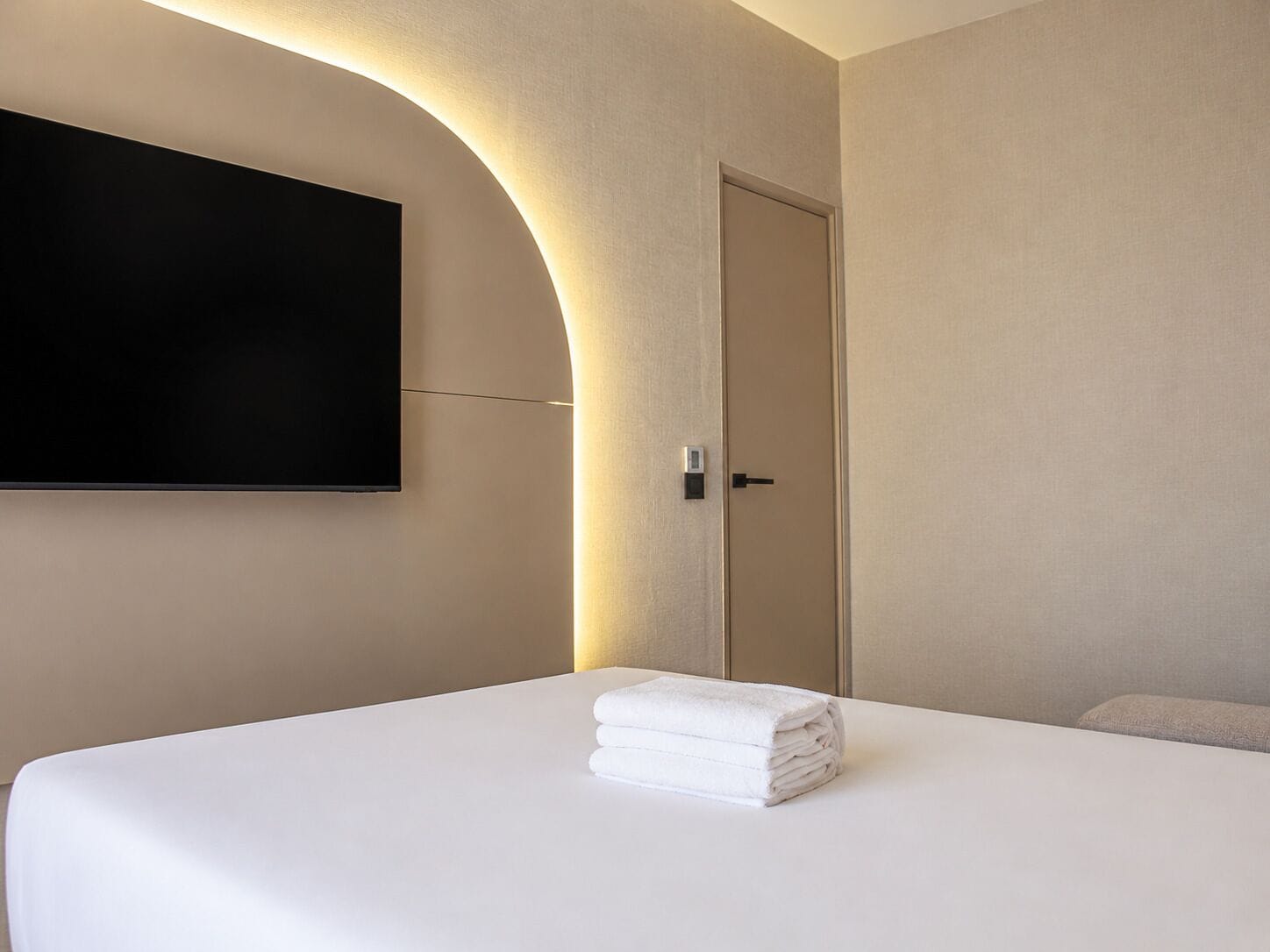 Habitació d'hotel amb un llit, una porta i un televisor fixat a la paret.