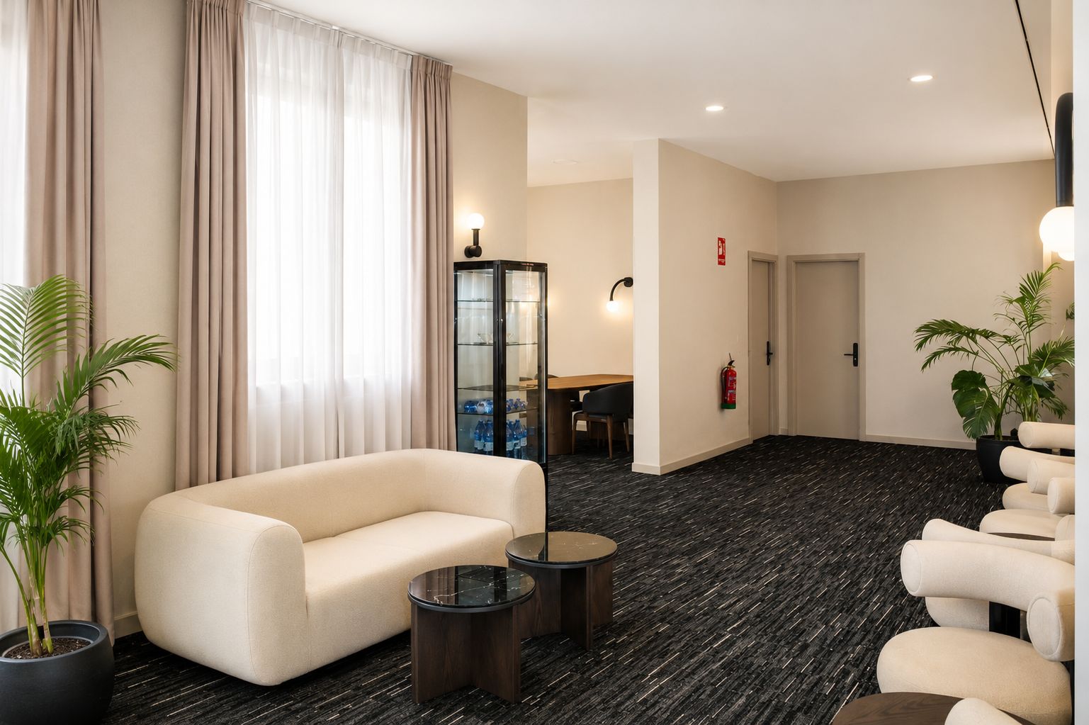 Eine Hotelhalle mit einer Couch, Sesseln, einem kleinen Tisch, einem Schrank und einem Feuerlöscher.