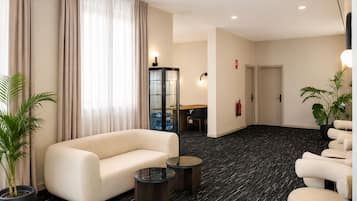 Een hotel lobby met een bank, fauteuils, een kleine tafel, een kast en een brandblusser.