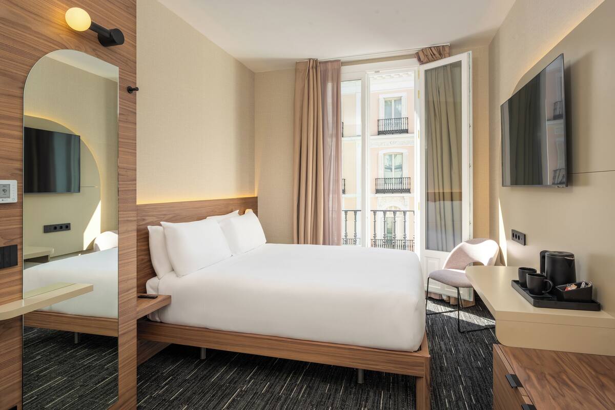 A hotel room with a bed, a desk, a chair, a TV, and a balcony view.