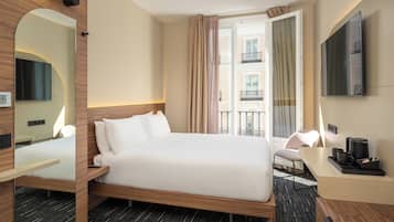 A hotel room with a bed, a desk, a chair, a TV, and a balcony view.