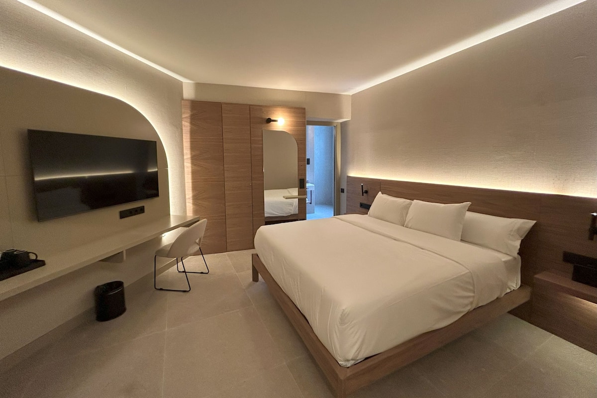 A modern hotel room with a large bed, a desk, and a TV mounted on the wall.