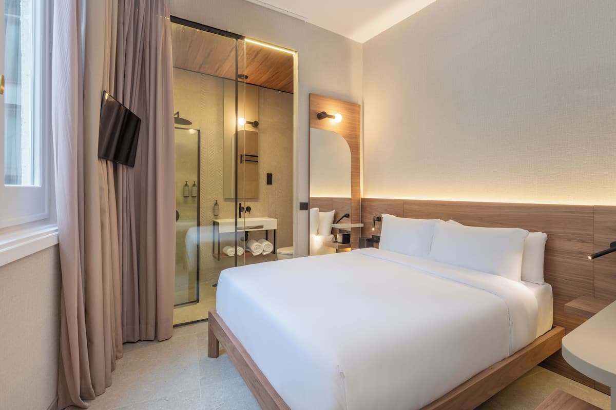 A modern hotel room with a large bed, a glass shower enclosure, and a wooden headboard.