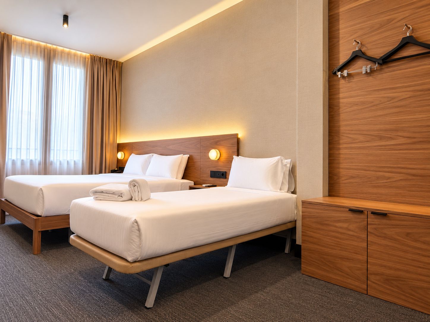 A hotel room with two beds, a wooden headboard, a wardrobe, and a coat rack.